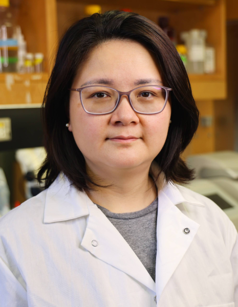 Woman with black hair and glasses wearing a white coat in a lab setting